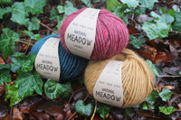 Three skeins of yarn in red, blue, and yellow on a leafy background